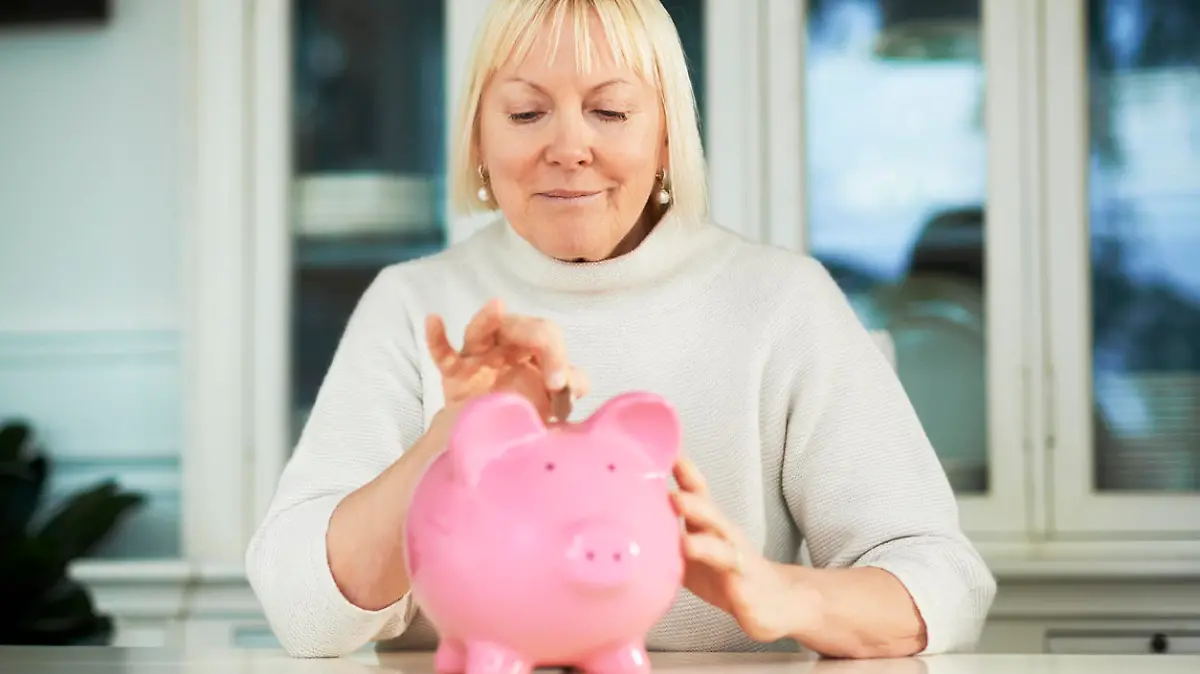 Eine Frau wirft Geld in ein Sparschwein.