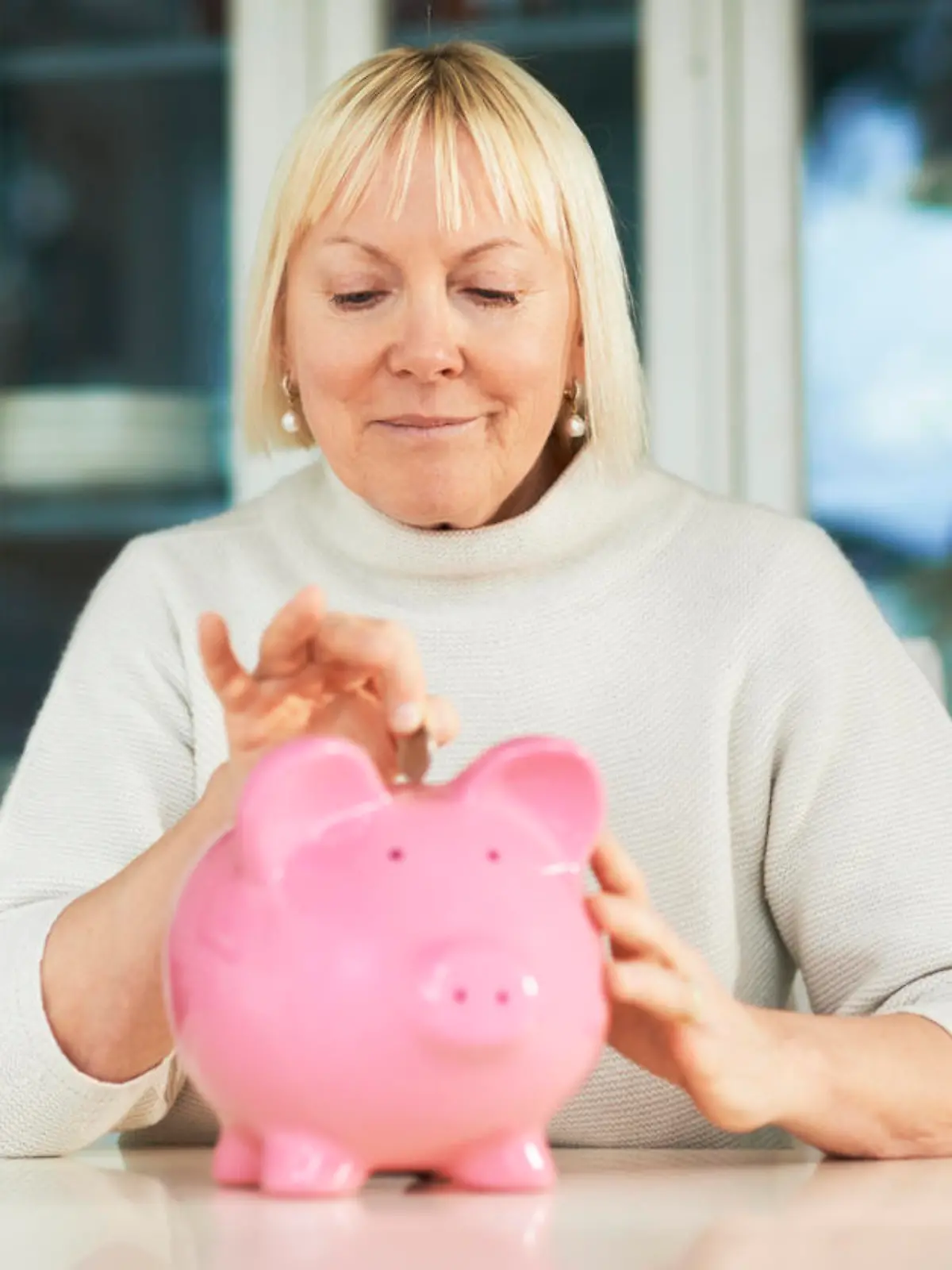 Eine Frau wirft Geld in ein Sparschwein.