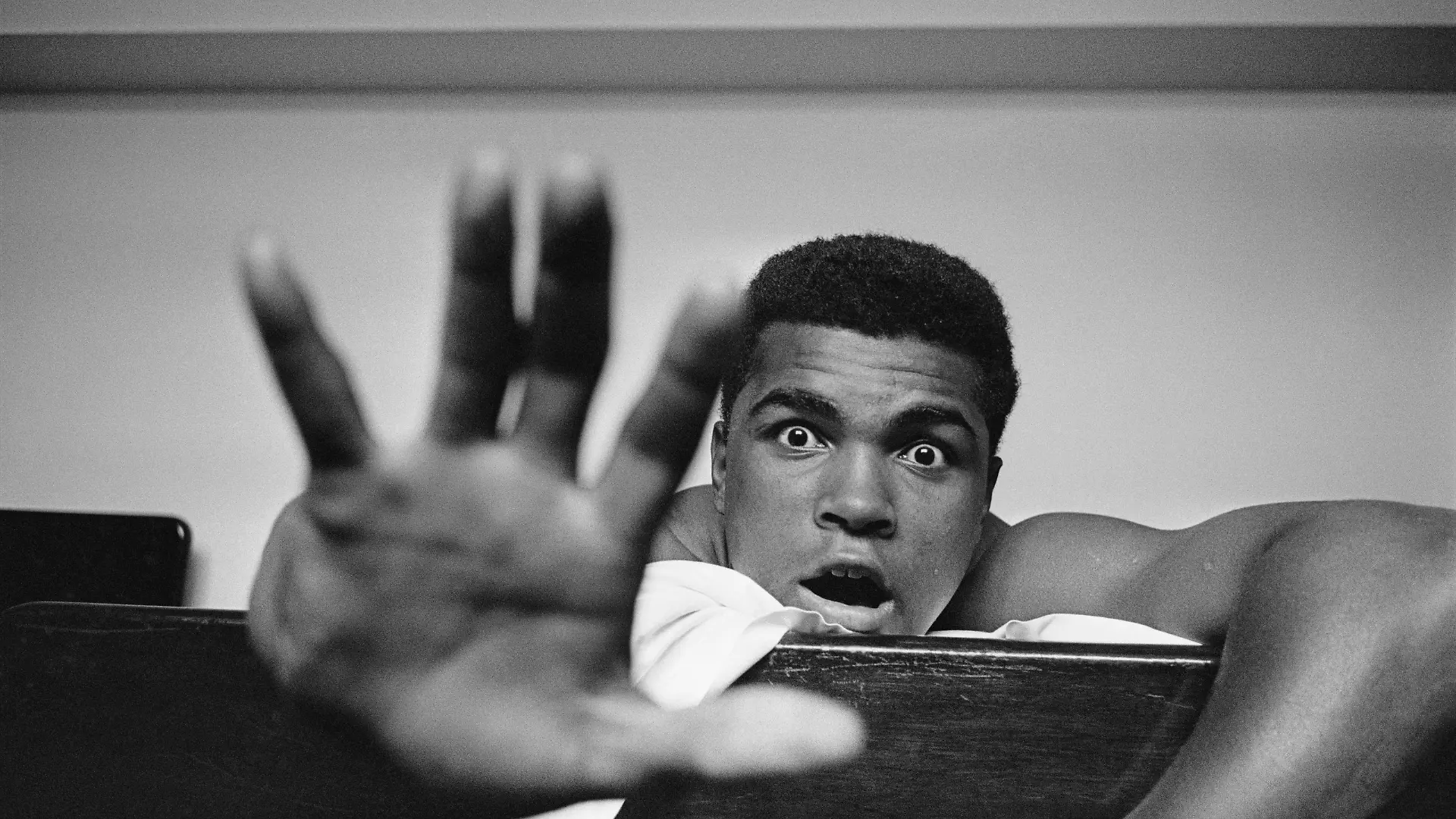 27th May 1963: American Heavyweight boxer Cassius Clay (later Muhammad Ali) lying on his hotel bed in London. He holds up five fingers in a prediction of how many rounds it will take him to knock out British boxer Henry Cooper. (Photo by Len Trievnor/Express/Getty Images)