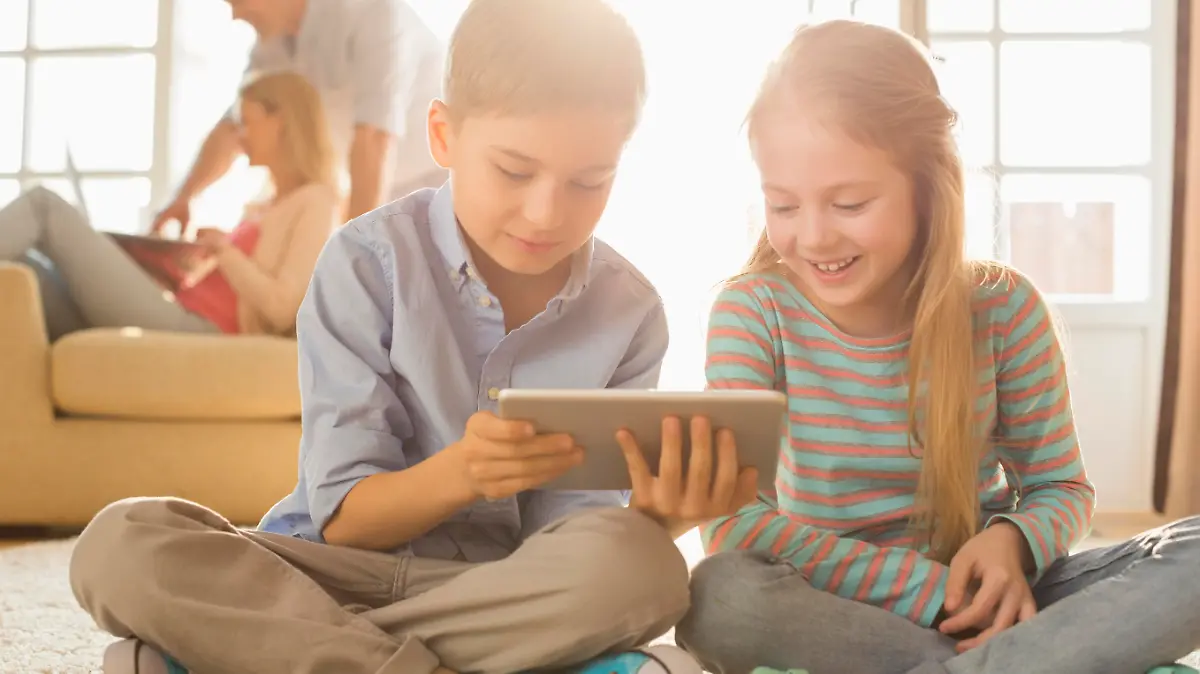 Happy siblings using digital tablet on floor with parents in background