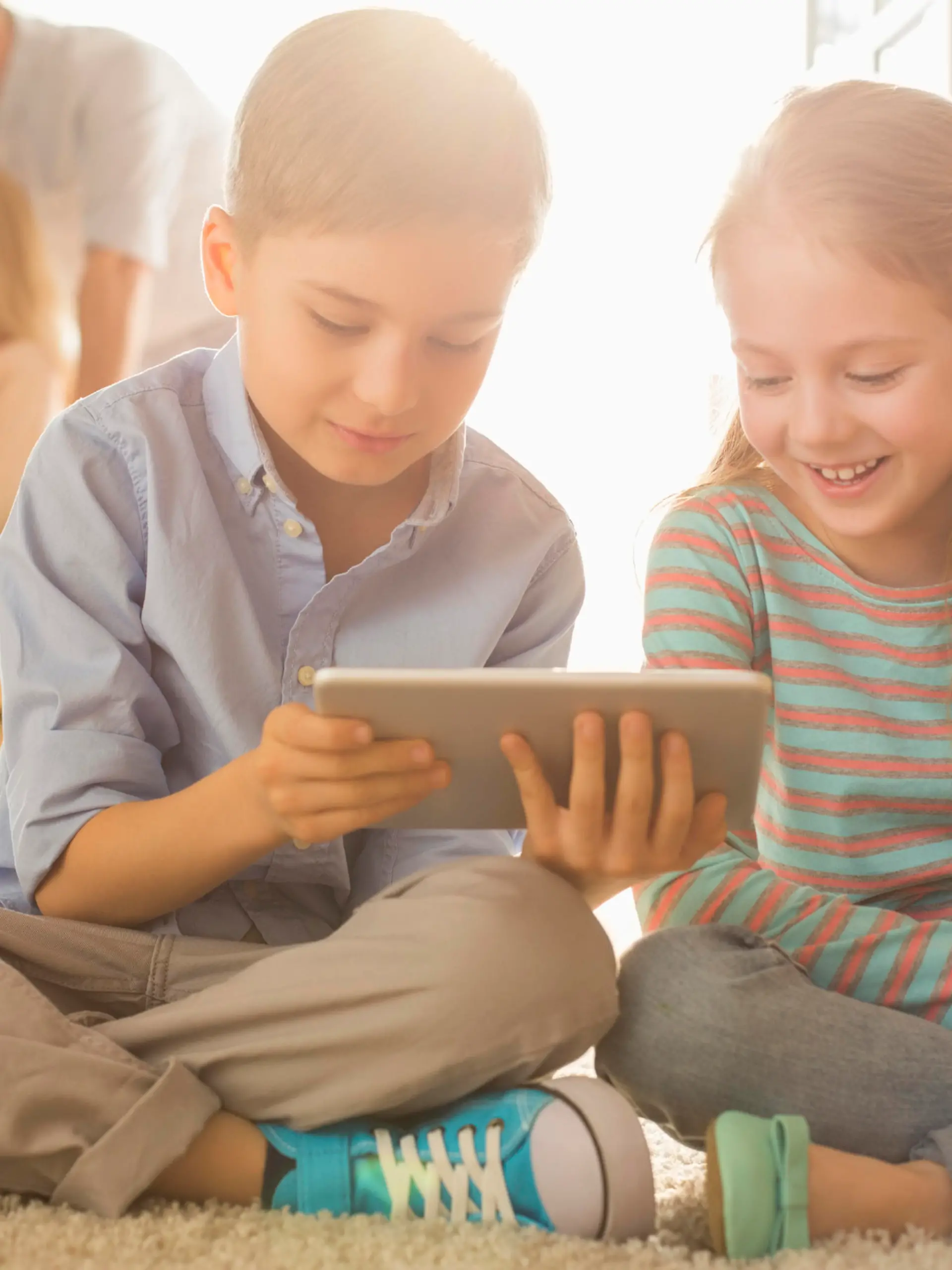 Happy siblings using digital tablet on floor with parents in background