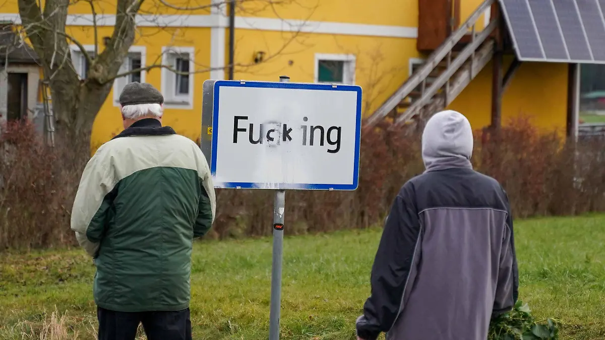 08.12.2020, Österreich, Fugging: Menschen kommen an einem Ortsschild vorbei, auf dem die Buchstaben «gg» mit «ck» übermalt wurden. Erst in der Vorwoche sind die neuen Ortsschilder der oberösterreichischen Ortschaft Fucking aufgestellt worden, die ab nächstem Jahr offiziell Fugging heißt. Doch der Frieden währte nicht lange. In der Nacht auf den 08.12.2020 wurde aus der neuen Schreibweise Fugging wieder Fucking. Unbekannte Täter haben die Ortstafeln mit schwarzem Lackspray beschmiert. Foto: Daniel Scharinger/APA/dpa +++ dpa-Bildfunk +++