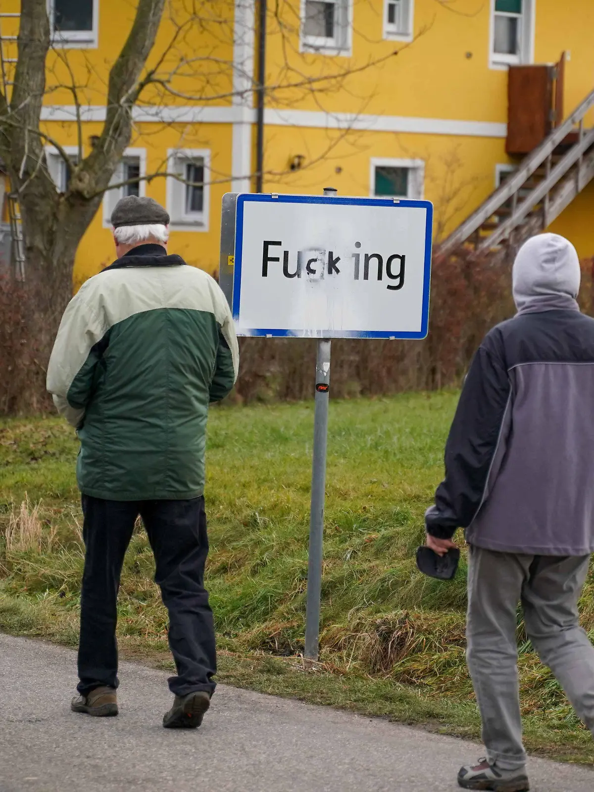 08.12.2020, Österreich, Fugging: Menschen kommen an einem Ortsschild vorbei, auf dem die Buchstaben «gg» mit «ck» übermalt wurden. Erst in der Vorwoche sind die neuen Ortsschilder der oberösterreichischen Ortschaft Fucking aufgestellt worden, die ab nächstem Jahr offiziell Fugging heißt. Doch der Frieden währte nicht lange. In der Nacht auf den 08.12.2020 wurde aus der neuen Schreibweise Fugging wieder Fucking. Unbekannte Täter haben die Ortstafeln mit schwarzem Lackspray beschmiert. Foto: Daniel Scharinger/APA/dpa +++ dpa-Bildfunk +++