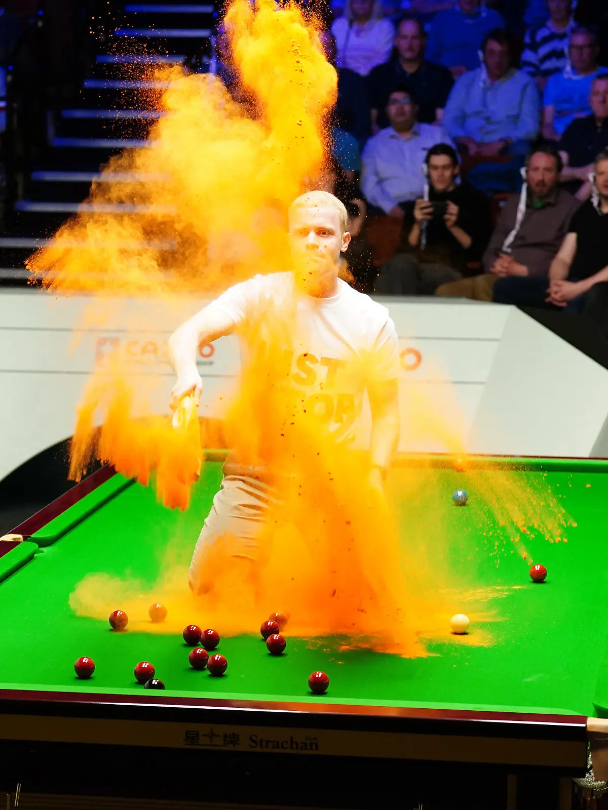 17.04.2023, Großbritannien, Sheffield: Snooker: WM, 1. Runde: Ein «Just Stop Oil»-Demonstrant springt auf den Tisch und wirft orangenes Pulver während des Spiels zwischen Milkins und Perry. Foto: Mike Egerton/PA Wire/dpa +++ dpa-Bildfunk +++