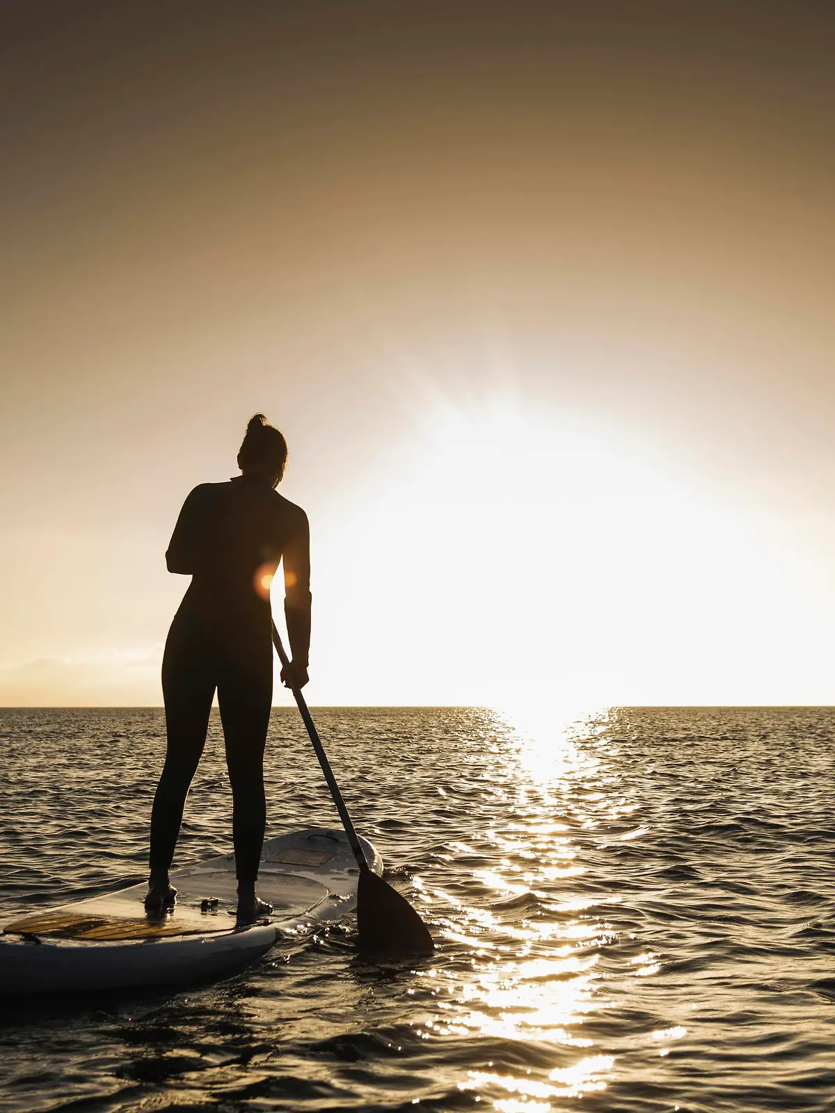 Young woman stand up paddle surfing at sunset || Modellfreigabe vorhanden
