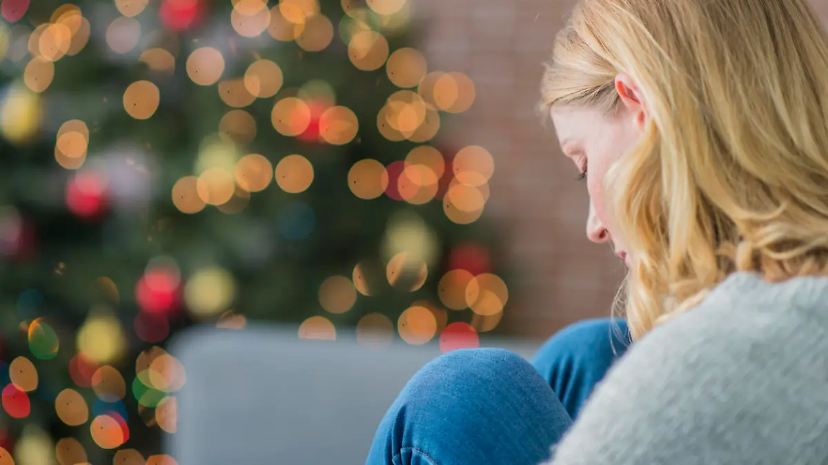Junge Frau sitzt traurig und allein vor dem Weihnachtsbaum