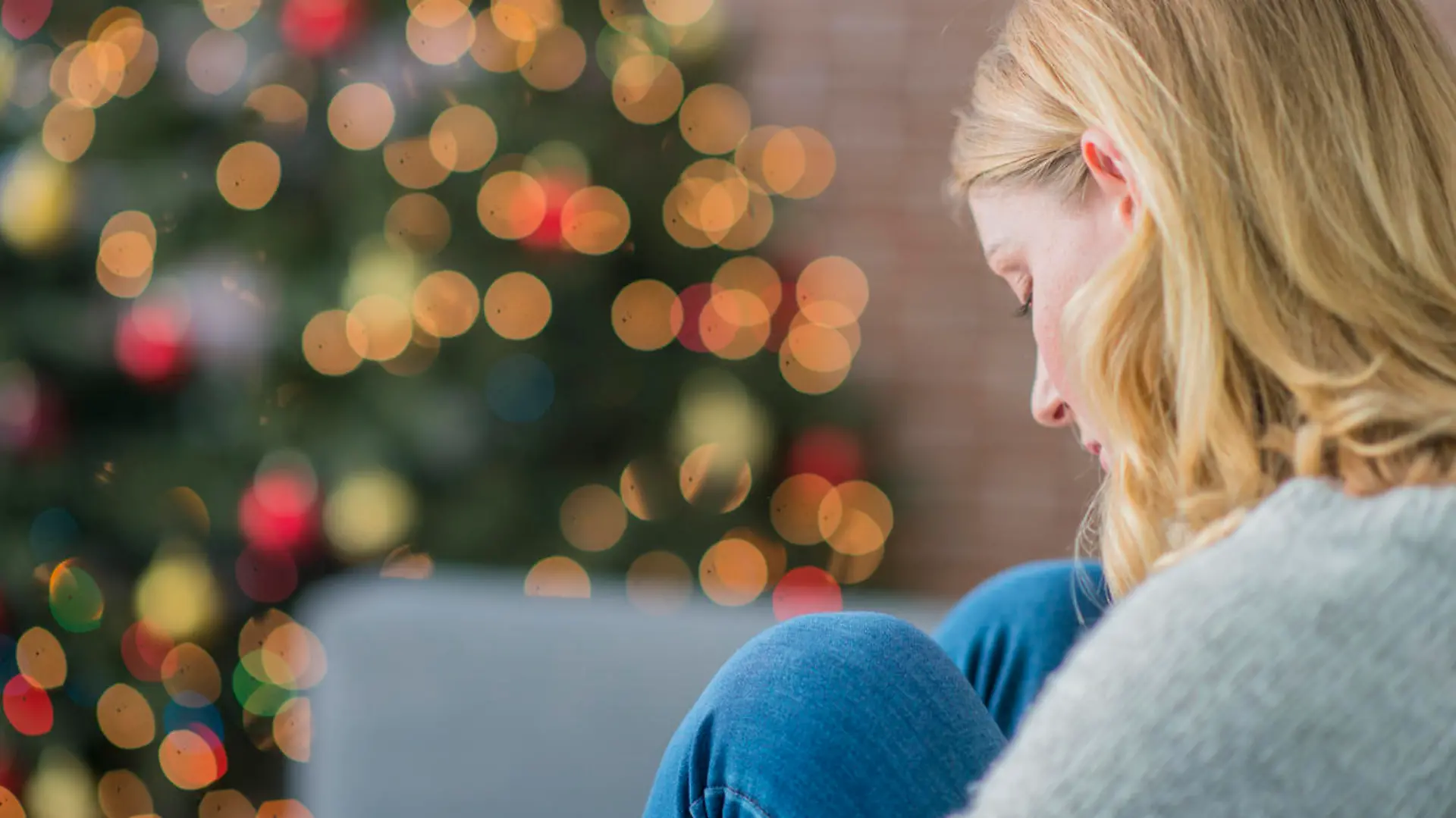 Junge Frau sitzt traurig und allein vor dem Weihnachtsbaum