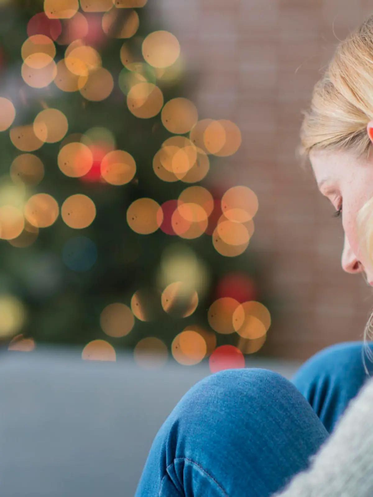 Junge Frau sitzt traurig und allein vor dem Weihnachtsbaum