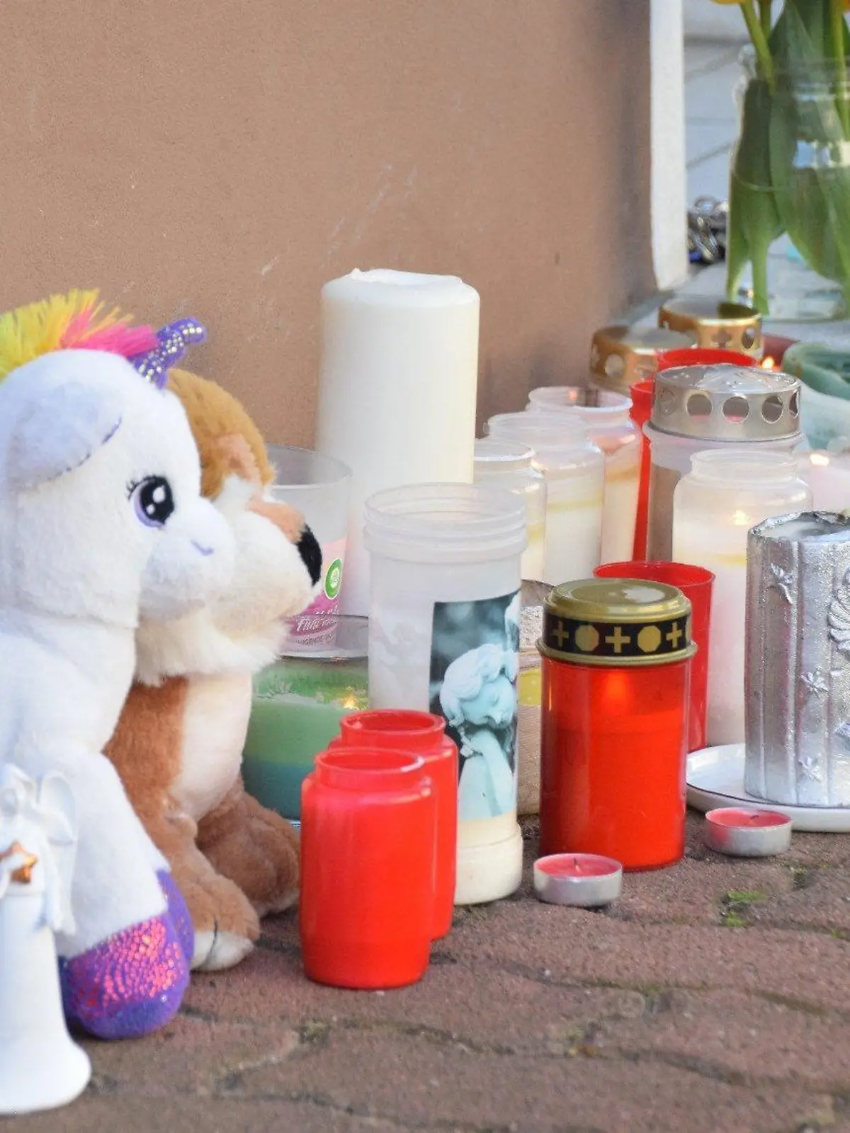 10.04.2023, Baden-Württemberg, Hockenheim: Plüschtiere und Kerzen stehen am Hauseingang zum Tatort in einer Wohnung. Im baden-württembergischen Hockenheim sind am Ostersonntag zwei Geschwister tot in einer Wohnung entdeckt worden. Die Kinder waren sieben und neun Jahre alt, wie die Staatsanwaltschaft und das Polizeipräsidium am Abend in Mannheim mitteilten. Foto: Marco Priebe/PR-Video/dpa +++ dpa-Bildfunk +++