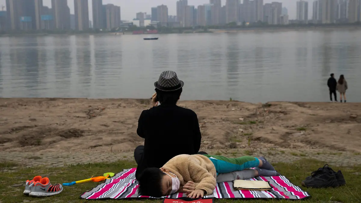 A child wearing a mask to protect against the coronavirus rests on the bank of the Yangtze River in Wuhan in central China's Hubei province on April 16, 2020. (AP Photo/Ng Han Guan)