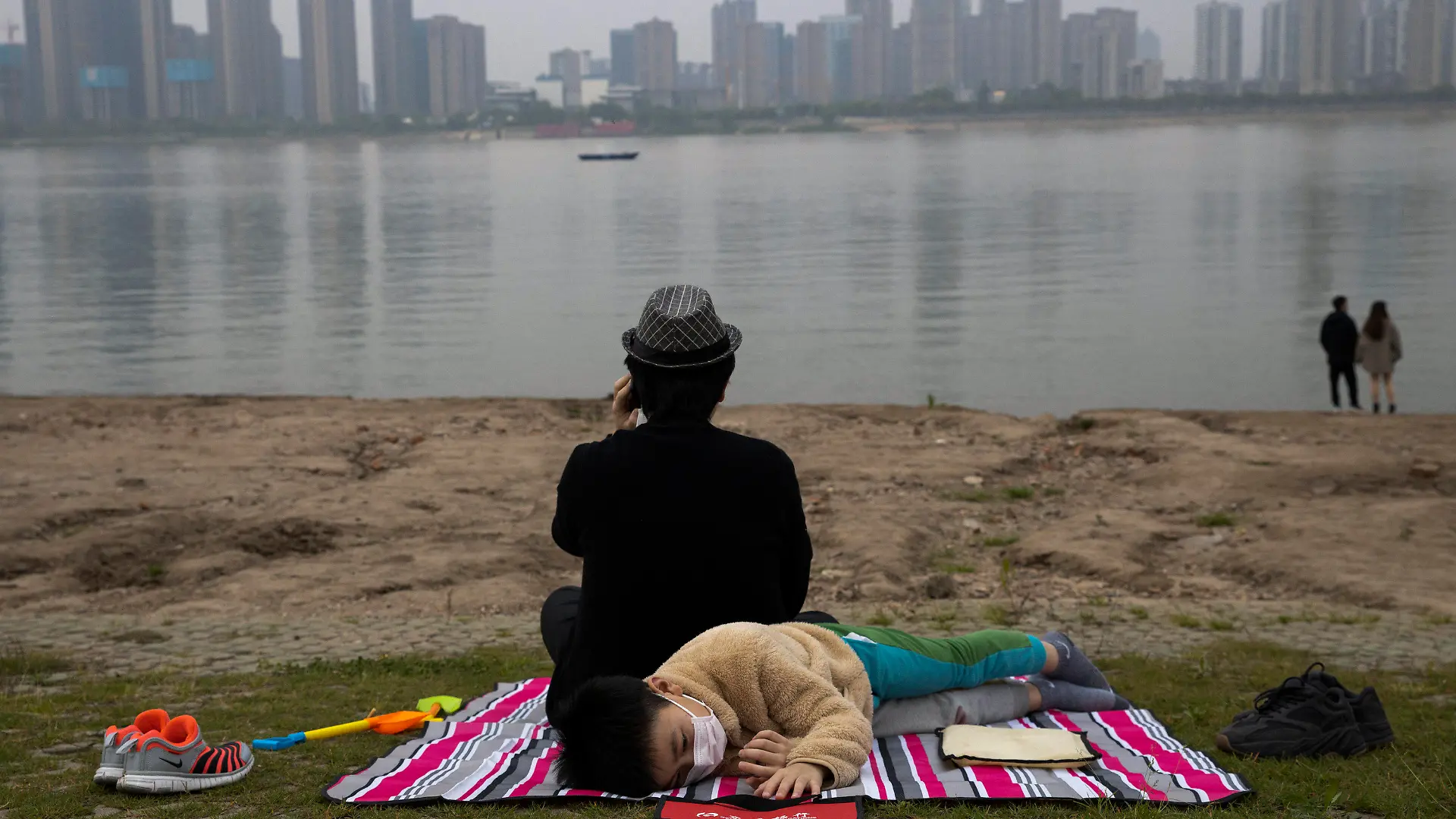 A child wearing a mask to protect against the coronavirus rests on the bank of the Yangtze River in Wuhan in central China's Hubei province on April 16, 2020. (AP Photo/Ng Han Guan)