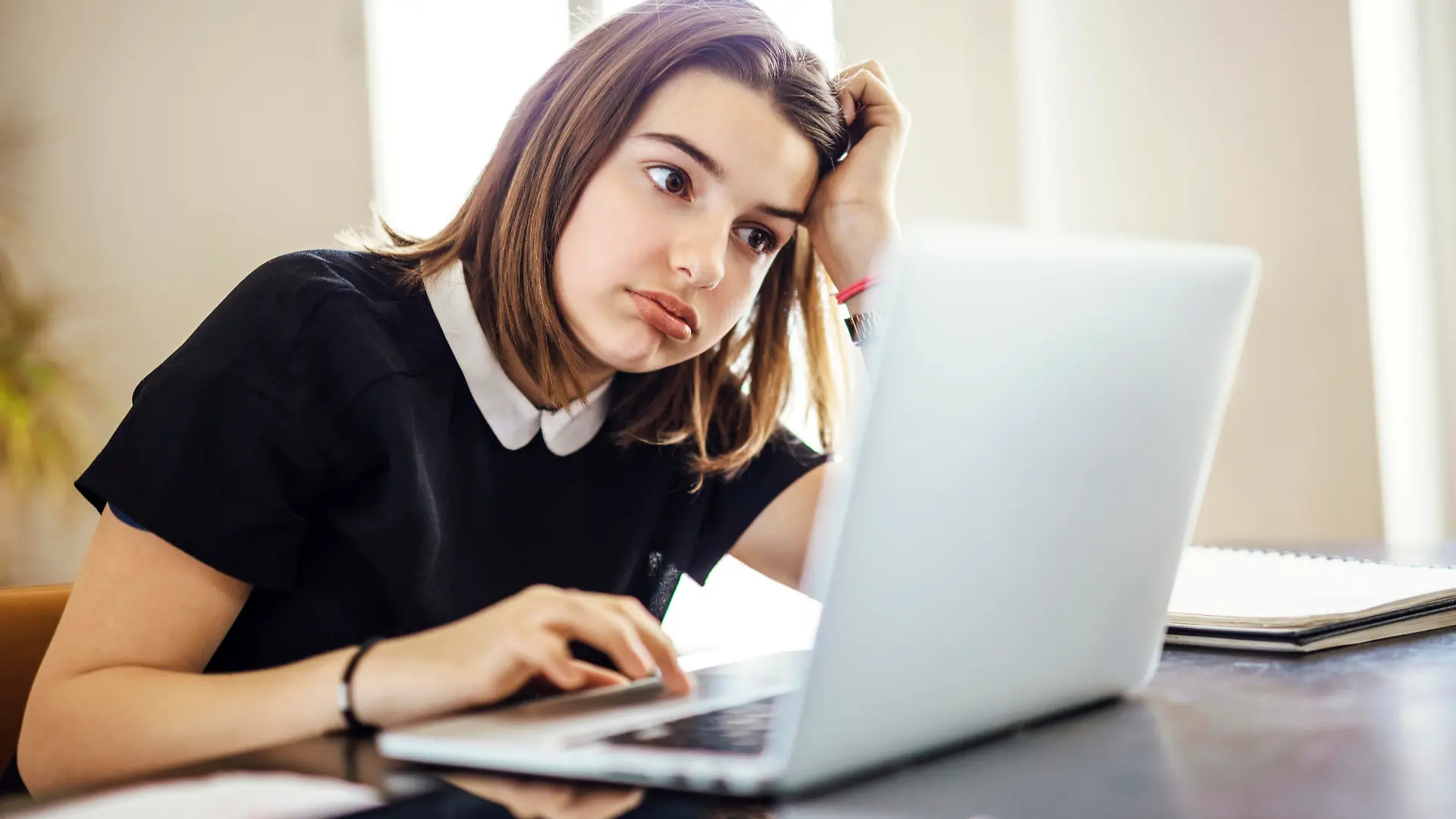 Frustrated youth using laptop computer trying to research something or finish homework on time while seated at desk with head resting on arm