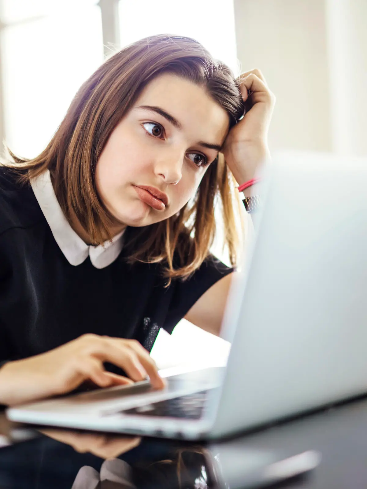 Frustrated youth using laptop computer trying to research something or finish homework on time while seated at desk with head resting on arm