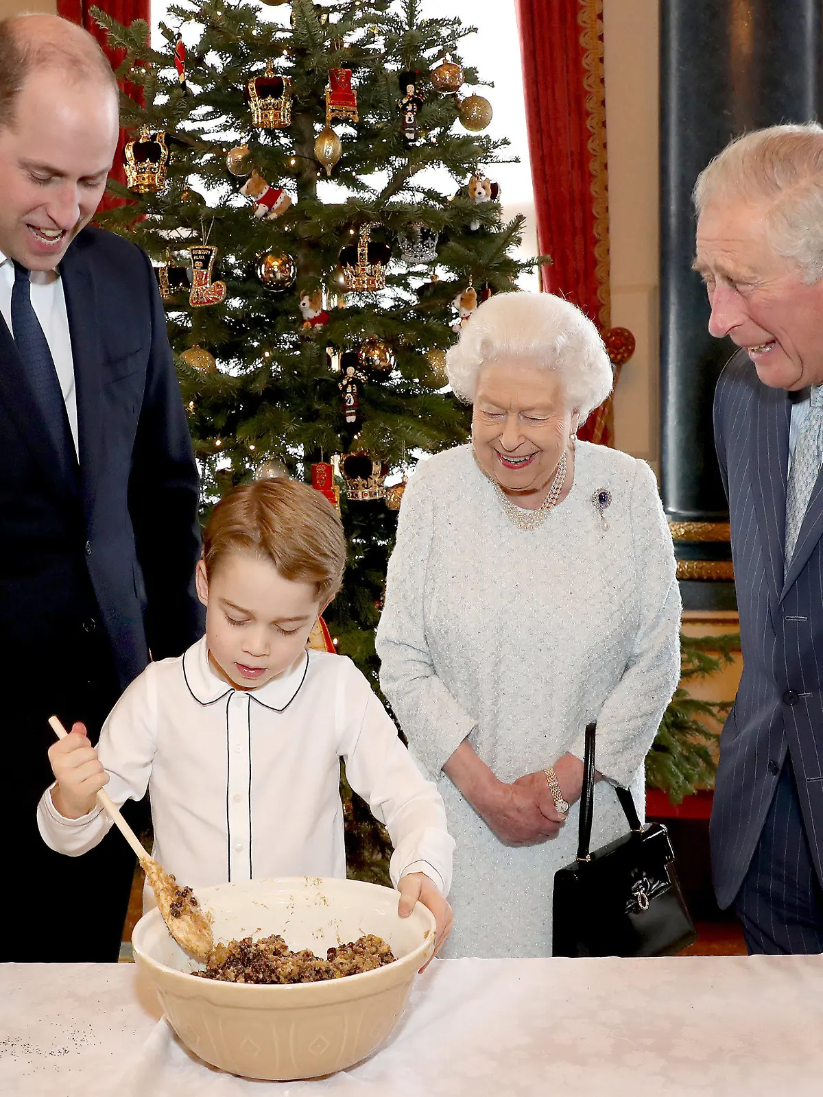 dpatopbilder - HANDOUT - 18.12.2019, Großbritannien, London: Die volle Aufmerksamkeit seines Vaters Prinz William (l), seiner Urgroßmutter Königin Elizabeth II. und seines Großvaters Prinz Charles (r) hat der kleine Prinz George bei der Zubereitung des traditionellen Christmas Puddings im Musikzimmer des Buckingham-Palasts. Die vorweihnachtliche Aktion fand im Rahmen der Initiative "The Royal British Legion's Together at Christmas" statt. Foto: Chris Jackson/Press Association Images/dpa - ACHTUNG: Honorarfrei. Nur zur redaktionellen Verwendung bis zum 05.01.2020 und nur mit vollständiger Nennung des vorstehenden Credits. Das Foto darf nicht bearbeitet oder verändert werden +++ dpa-Bildfunk +++