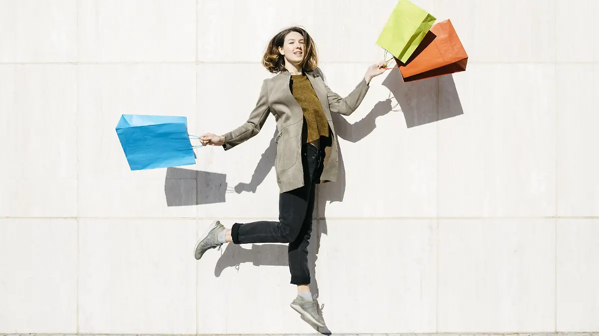  Cheerful woman with shopping bags jumping at a wall model released Symbolfoto PUBLICATIONxINxGERxSUIxAUTxHUNxONLY JRFF02783