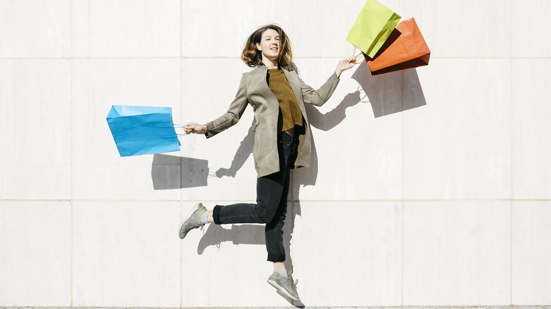 Cheerful woman with shopping bags jumping at a wall model released Symbolfoto PUBLICATIONxINxGERxSUIxAUTxHUNxONLY JRFF02783