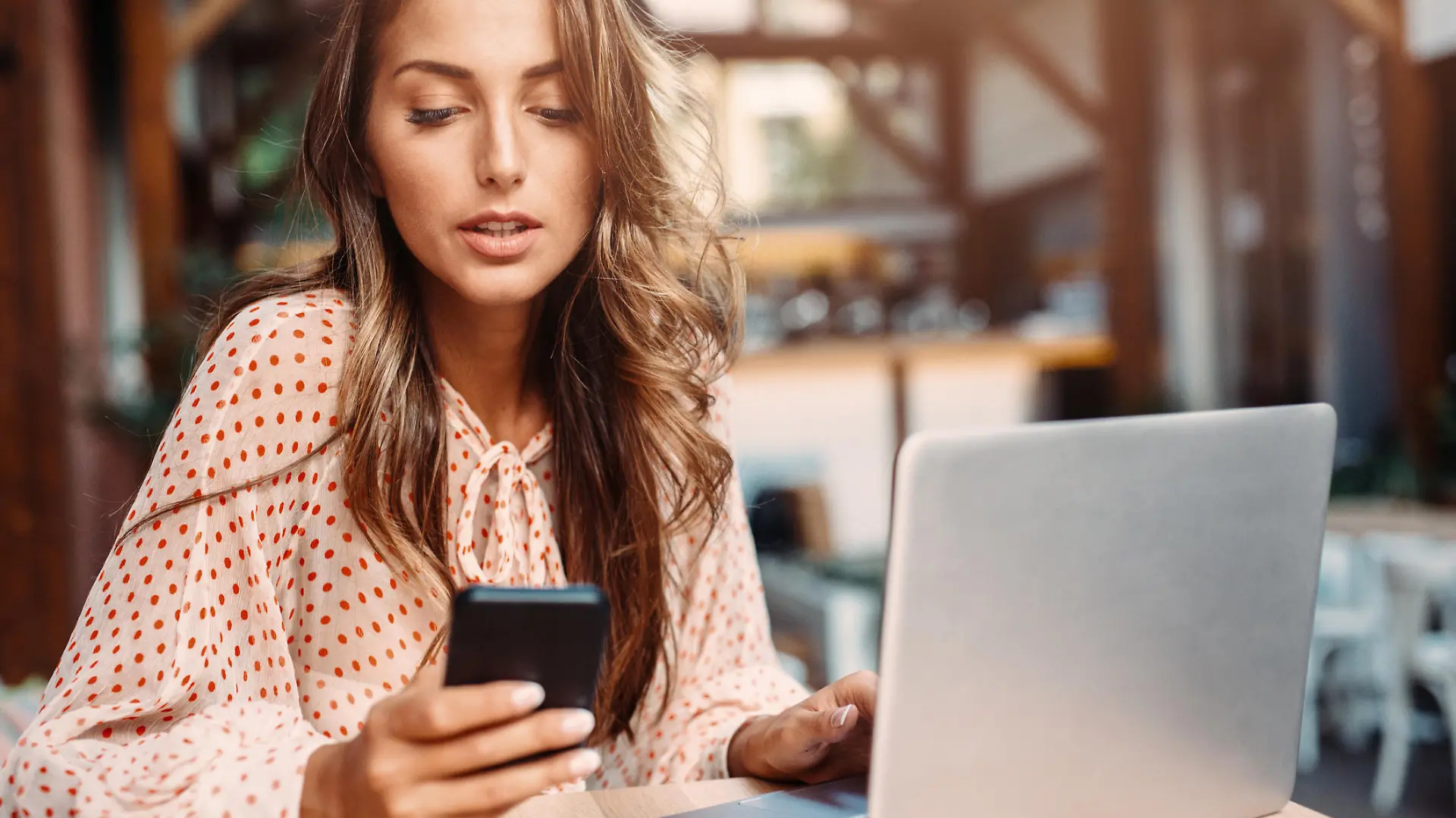 Young lady texting while using a laptop at the cafe.