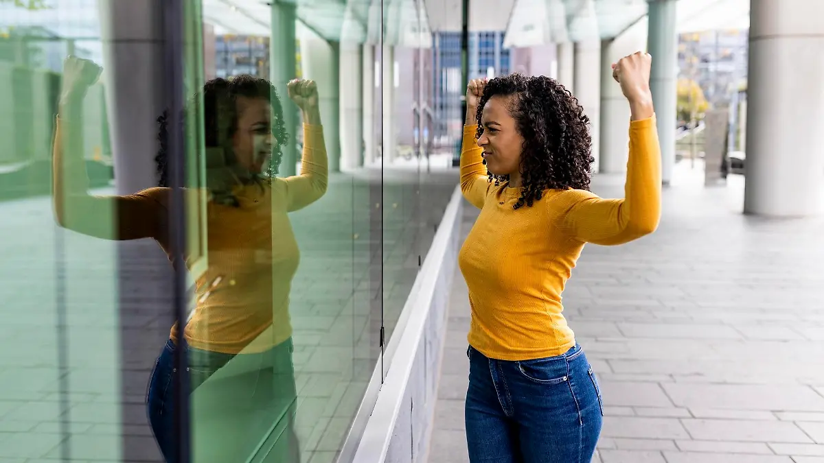 Woman flexing muscles looking reflection on glass wall || Modellfreigabe vorhanden