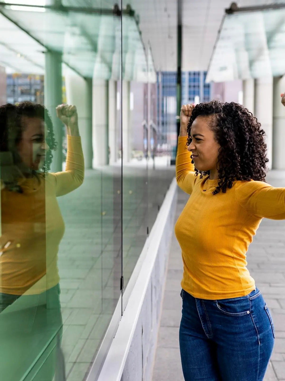 Woman flexing muscles looking reflection on glass wall || Modellfreigabe vorhanden