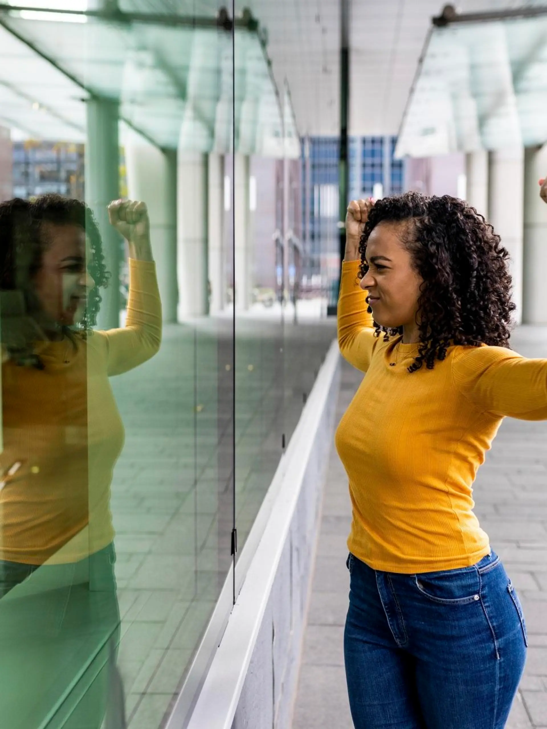 Woman flexing muscles looking reflection on glass wall || Modellfreigabe vorhanden
