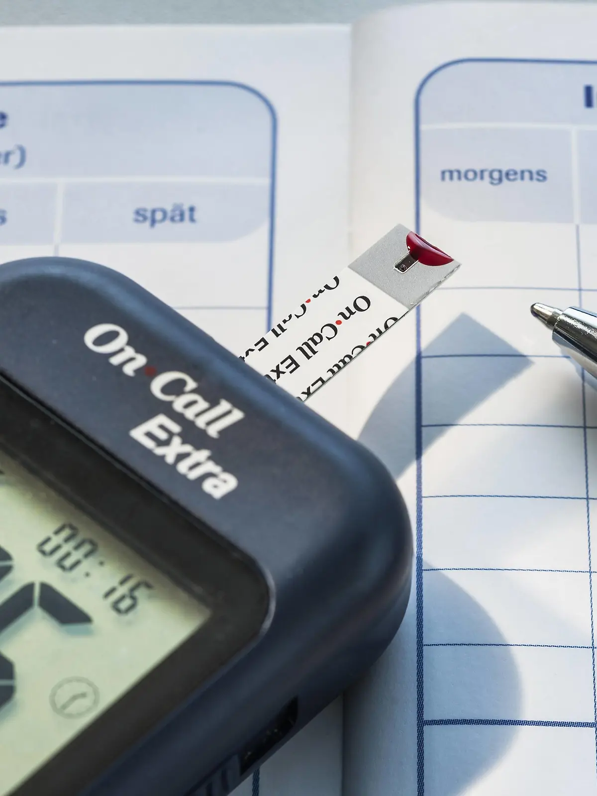  Symbolbild Diabetes, Messgerät zur Blutzuckerbestimmung mit einem Bluttropfen auf dem Messstreifen liegt auf einem Diabetes-Tagebuch Blutzuckerkontrolle *** Icon image Diabetes meter for measuring blood sugar with a drop of blood on the measuring strip lies on a diabetes diary blood sugar control