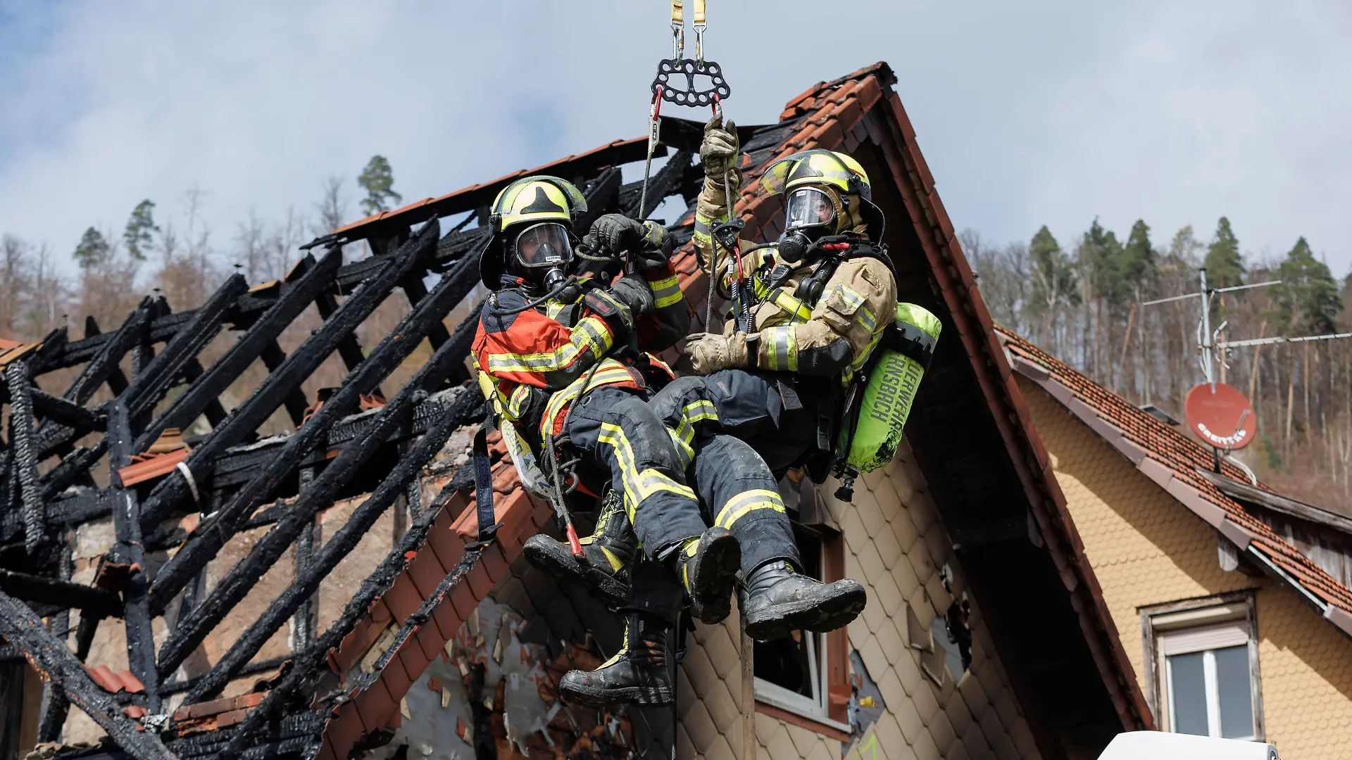 13.04.2023, Baden-Württemberg, Gernsbach: Zwei Feuerwehrleute werden mit Hilfe einer Drehleiter aus dem ausgebrannten Dachstuhl herausgehoben. Am frühen Morgen ist eine zum Wohnhaus umgebaute ehemalige Gaststätte in Gernsbach in Brand geraten. Einige Bewohner konnten gerettet werde, während mehrere Personen am Vormittag noch als vermisst gelten. Foto: Julian Rettig/dpa +++ dpa-Bildfunk +++