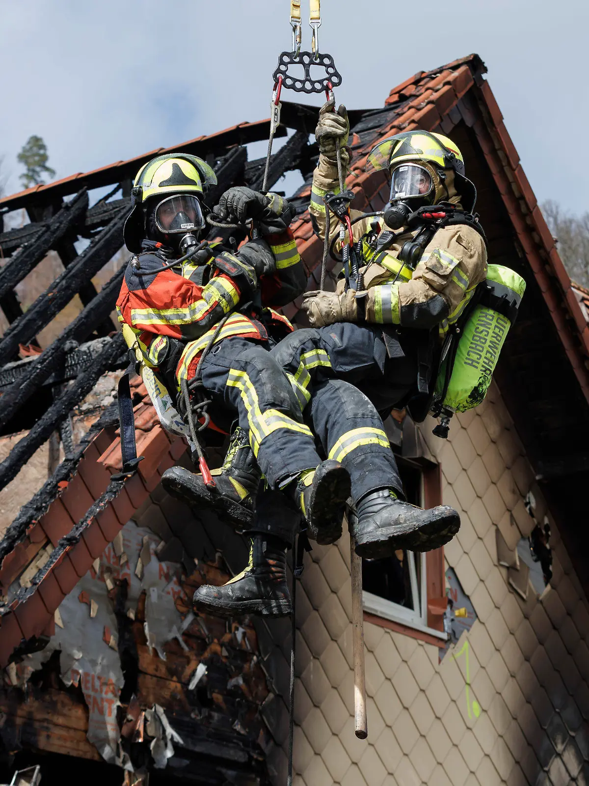 13.04.2023, Baden-Württemberg, Gernsbach: Zwei Feuerwehrleute werden mit Hilfe einer Drehleiter aus dem ausgebrannten Dachstuhl herausgehoben. Am frühen Morgen ist eine zum Wohnhaus umgebaute ehemalige Gaststätte in Gernsbach in Brand geraten. Einige Bewohner konnten gerettet werde, während mehrere Personen am Vormittag noch als vermisst gelten. Foto: Julian Rettig/dpa +++ dpa-Bildfunk +++