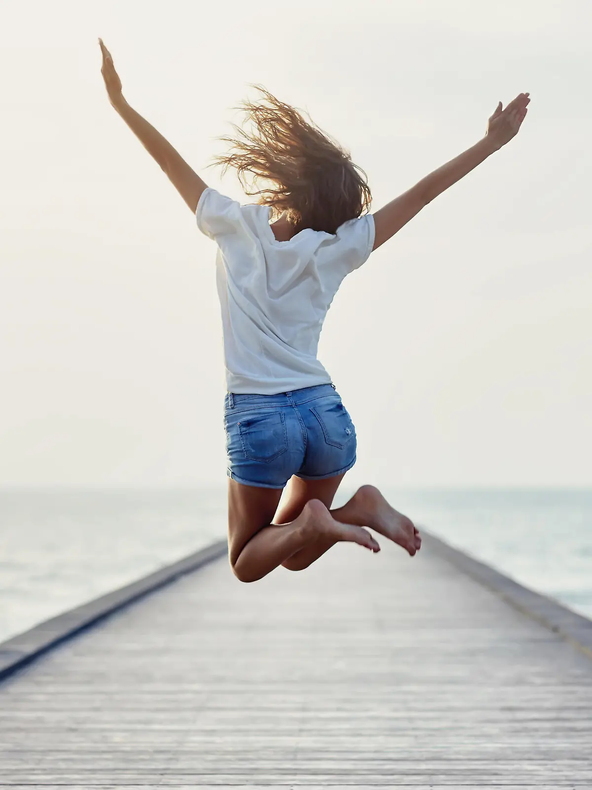 Back view of jumping girl on the pier. Freedom concept