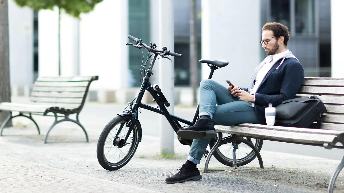 Mann mit Urban-E-Bike tippt ins Handy.