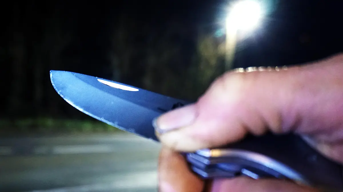 Kriminalität, Raub und Überfall / Raubüberfall - Symbolbilder Angriff mit Messer / Messerangriff - Symbolbilder .Messer als Kampfmittel und Waffe Eine Person hält bei Dunkelheit an einer Straße ein Messer in der Hand. *** Knife as a combat device and weapon A person holds a knife in his hand in the dark on a street