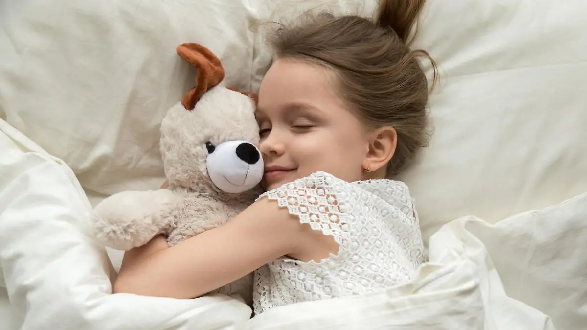 Mädchen kuschelt mit Stofftier im Bett