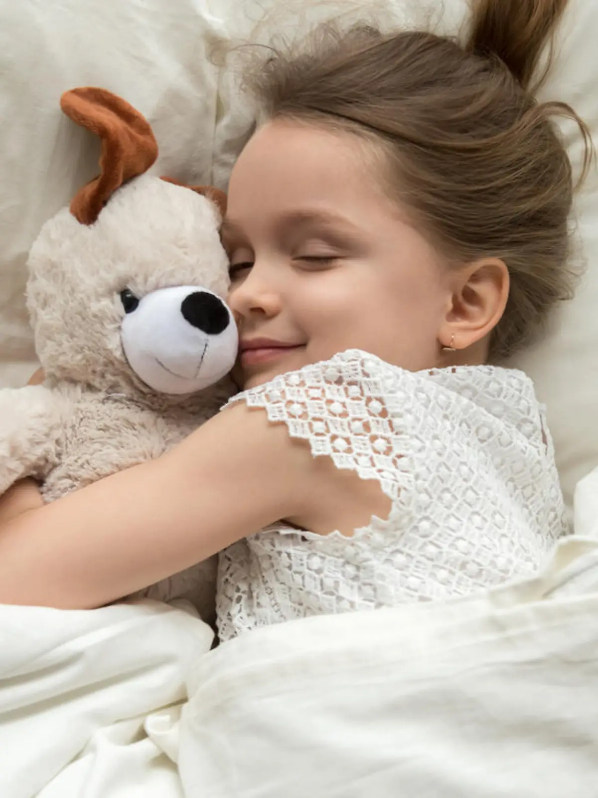 Mädchen kuschelt mit Stofftier im Bett