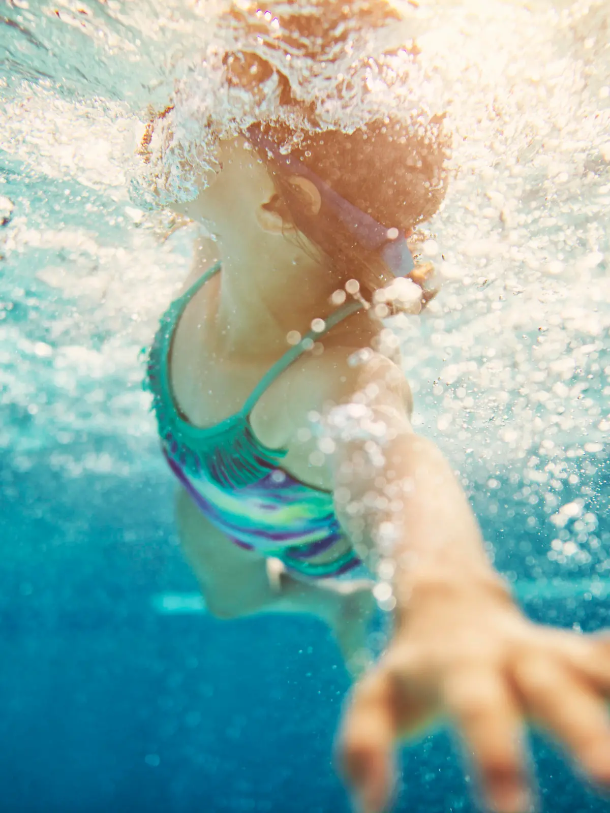 Little girl swimming crawl. Shot from underwater.  The girl is reaching towards the camera and taking a breath.