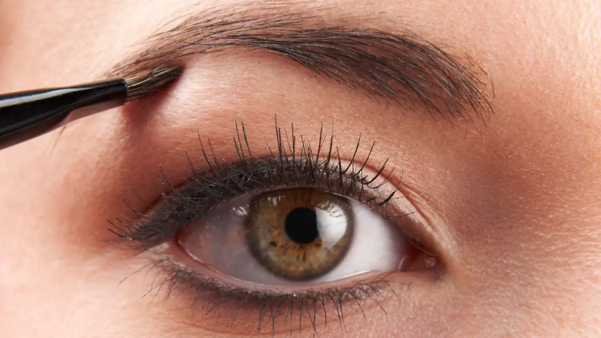woman applying eye make-up with brush on white background