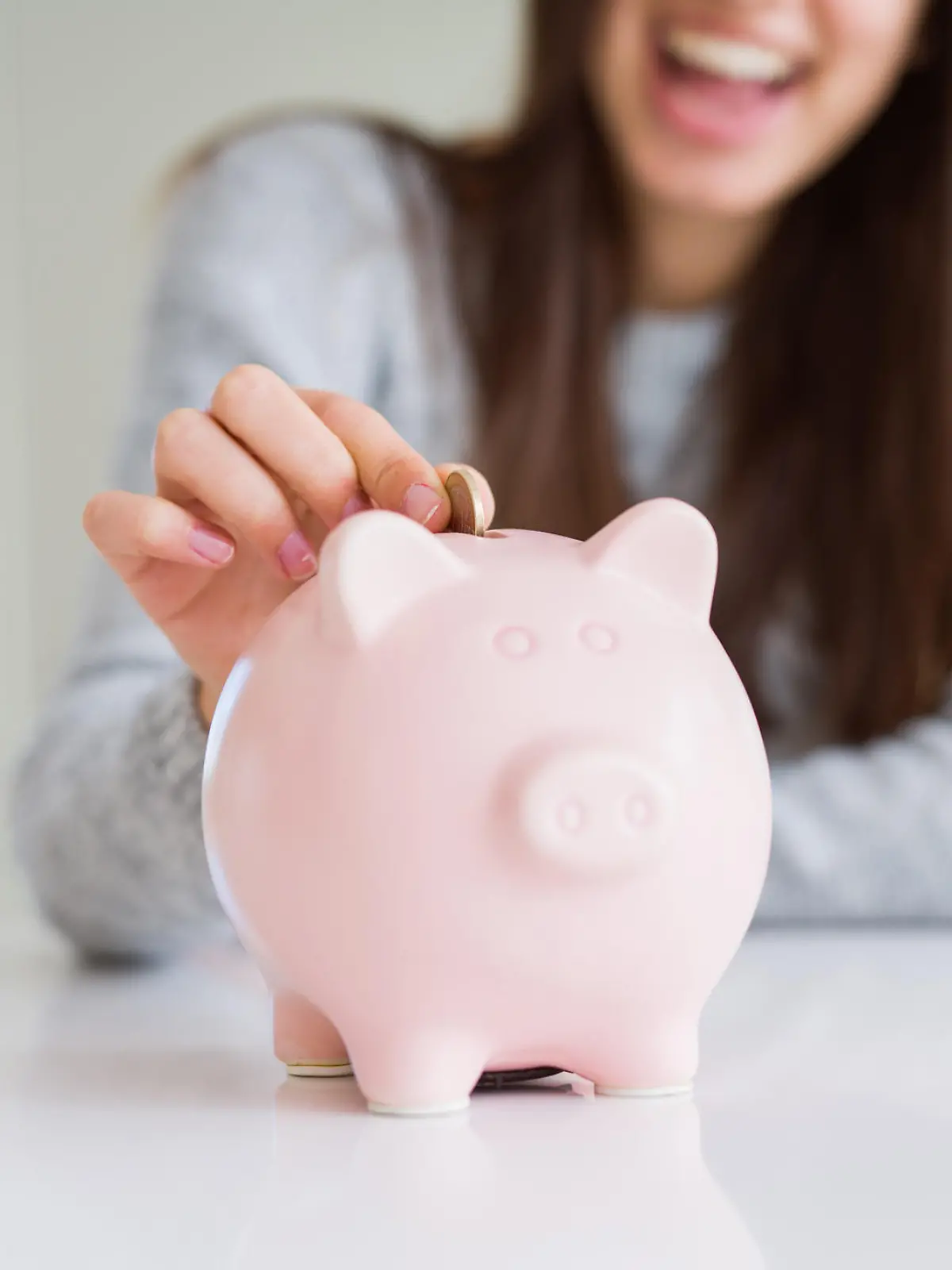 Young woman smiling putting a coin inside piggy bank as savings for investment