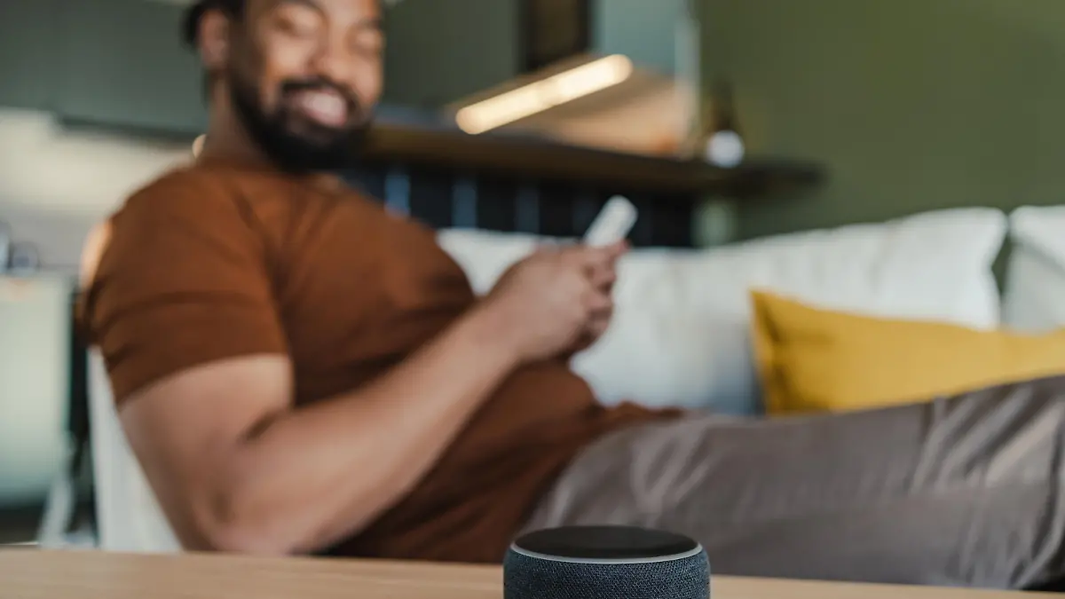Young African American man sitting on the couch and using his smart speaker and mobile phone