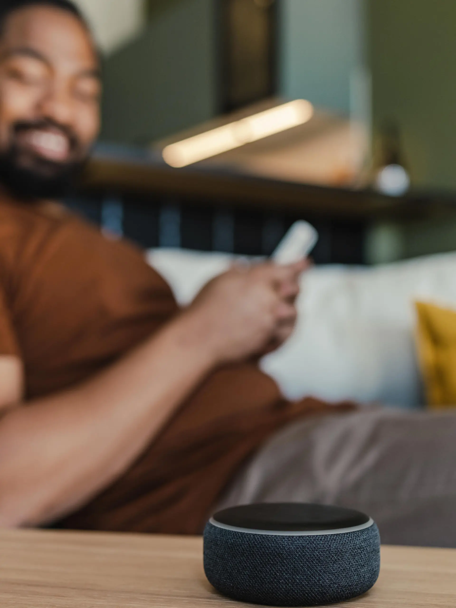 Young African American man sitting on the couch and using his smart speaker and mobile phone