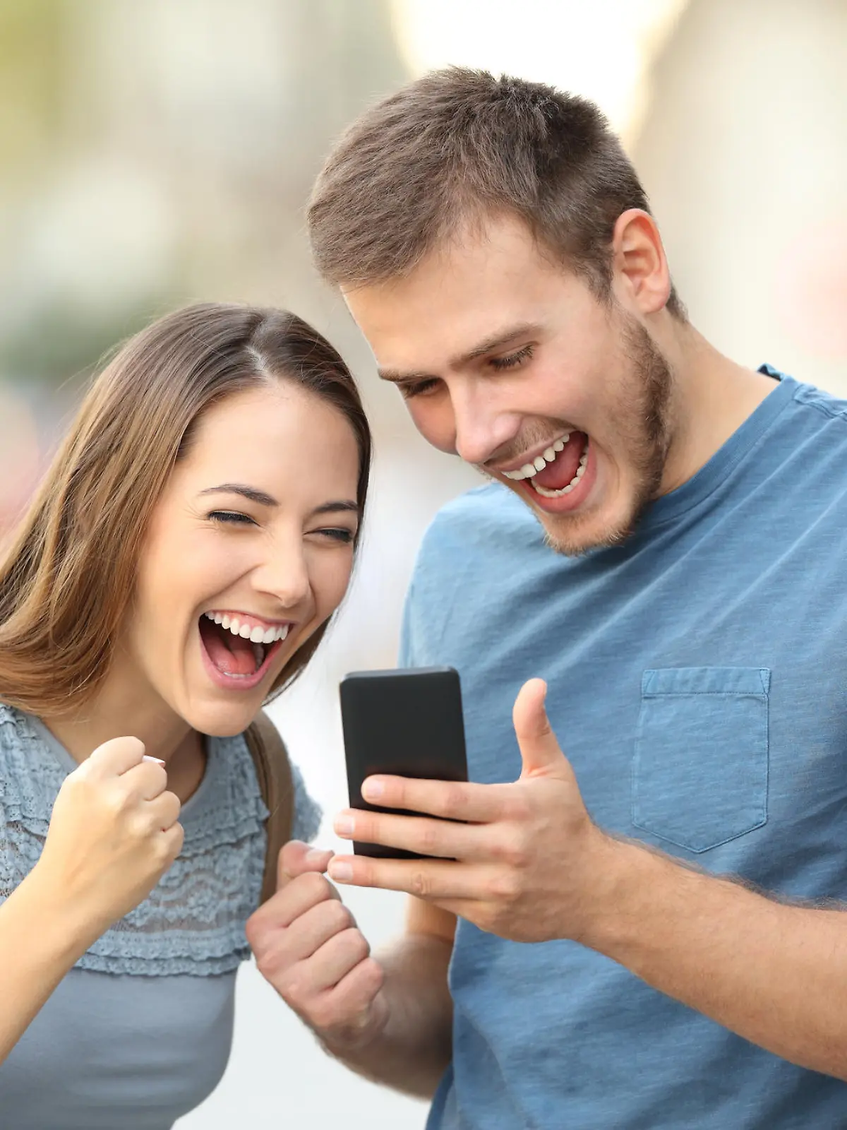 Excited couple receiving good news on line in a smart phone outside on the street