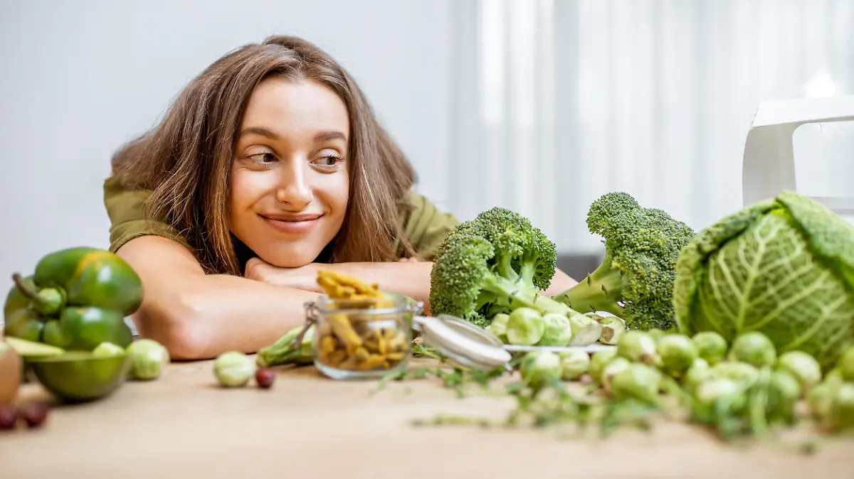 Portrait of a young cheerful woman with lots of healthy green food on the table. Concept of vegetarianism and well-being