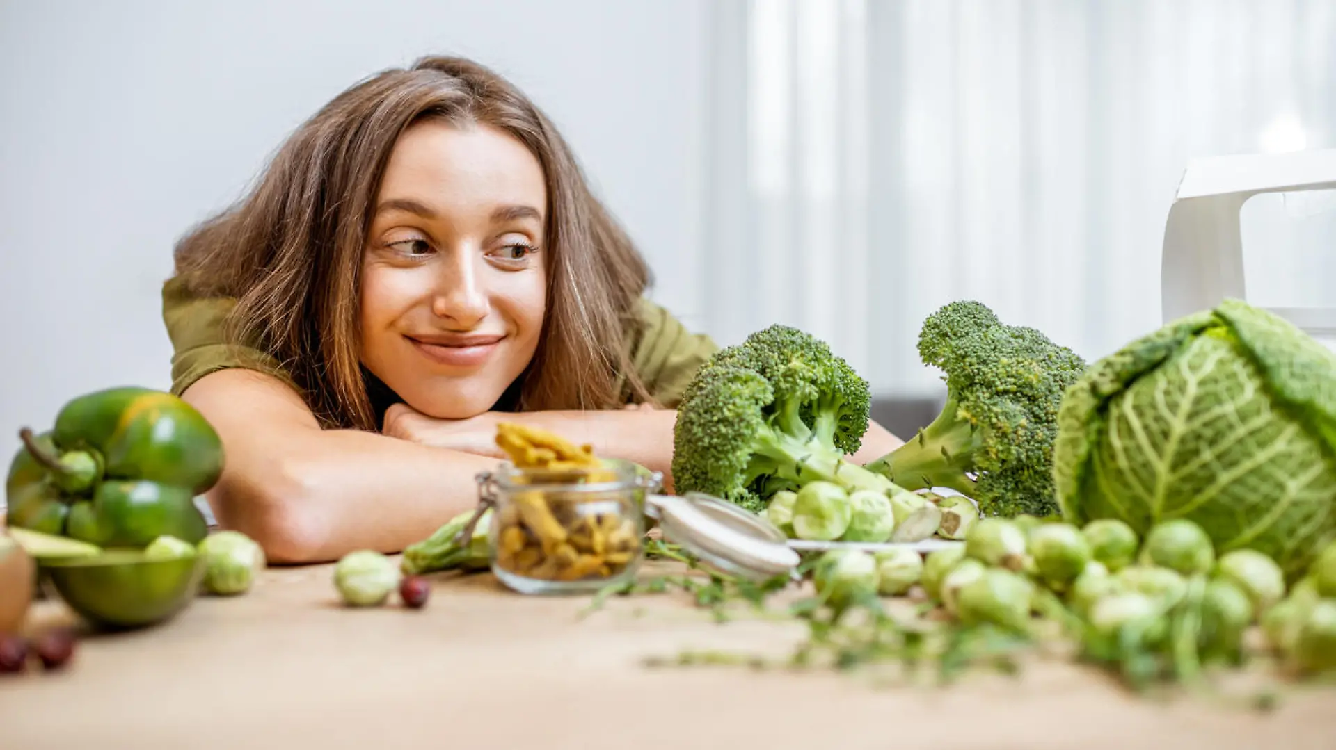 Portrait of a young cheerful woman with lots of healthy green food on the table. Concept of vegetarianism and well-being