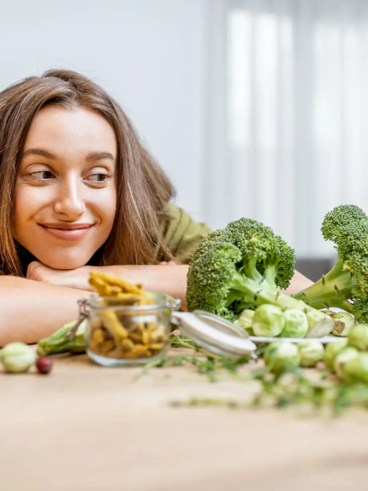 Portrait of a young cheerful woman with lots of healthy green food on the table. Concept of vegetarianism and well-being