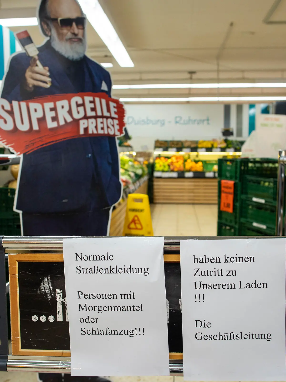 Auf einem Schild am Markteingang steht "Personen mit Morgenmantel oder Schlafanzug haben keinen Zutritt zu unserem Laden"