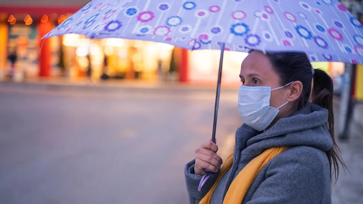 Frau mit Mund-Nasen-Maske und Regenschirm