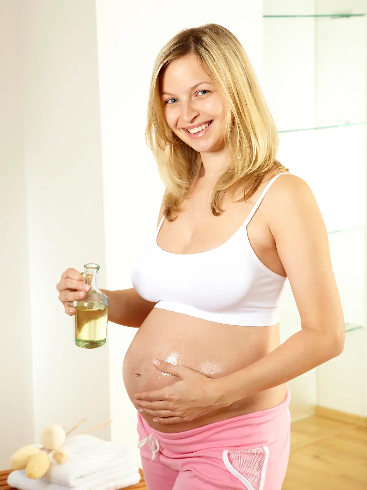 Frau reibt sich den Babybauch mit Öl ein