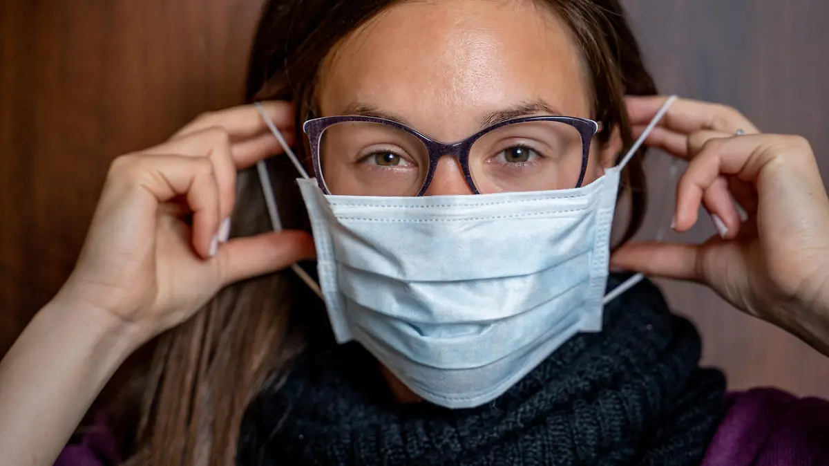 Junge Frau mit Brille zieht Maske auf