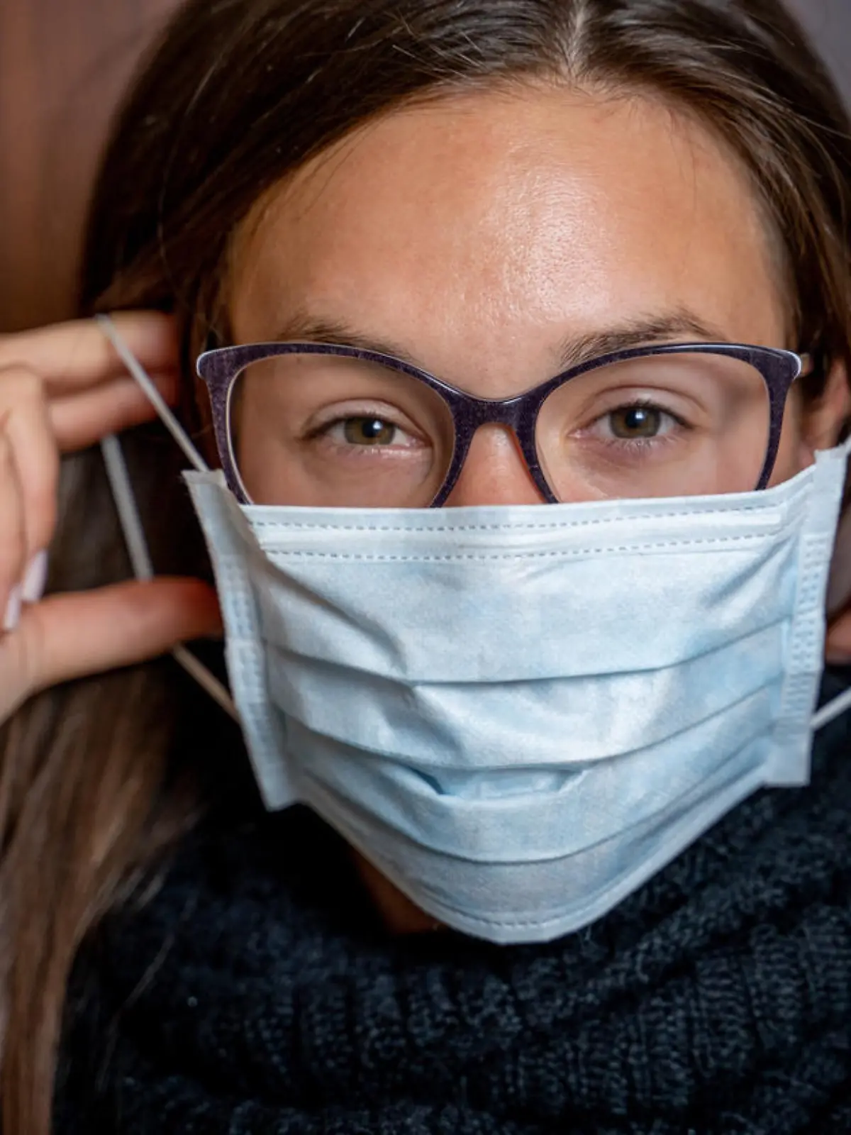 Junge Frau mit Brille zieht Maske auf