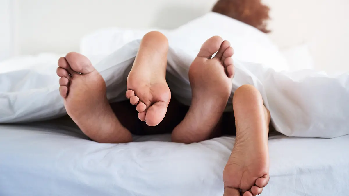 Paar liegt im Bett und die Füße gucken hervor.