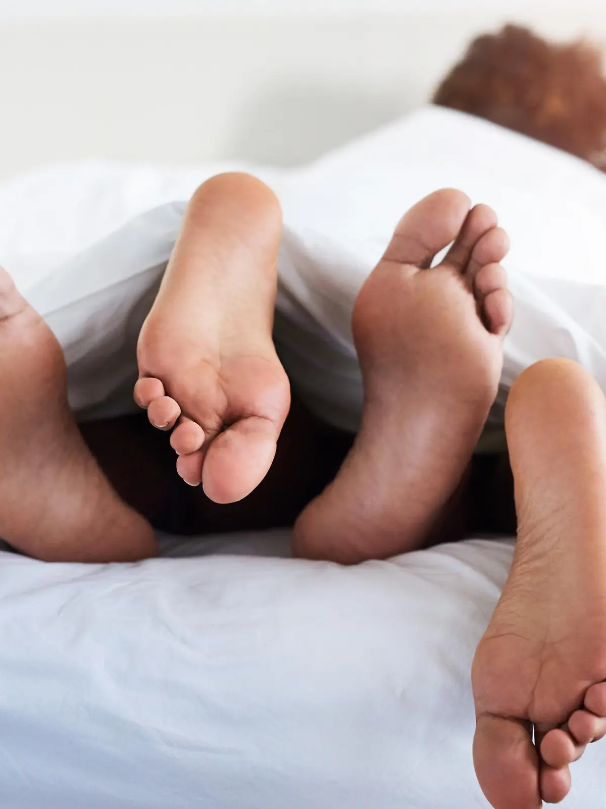 Paar liegt im Bett und die Füße gucken hervor.