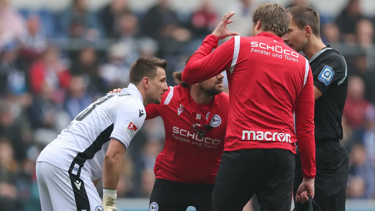 09.04.2023, Nordrhein-Westfalen, Bielefeld: Fußball: 2. Bundesliga, Arminia Bielefeld - Fortuna Düsseldorf, 27. Spieltag in der Schüco-Arena. Fans von Düsseldorf haben einen lauten Böller gezündet. Bielefelds Torwart Martin Fraisl (l) wird darauf hin behandelt. Foto: Friso Gentsch/dpa - WICHTIGER HINWEIS: Gemäß den Vorgaben der DFL Deutsche Fußball Liga bzw. des DFB Deutscher Fußball-Bund ist es untersagt, in dem Stadion und/oder vom Spiel angefertigte Fotoaufnahmen in Form von Sequenzbildern und/oder videoähnlichen Fotostrecken zu verwerten bzw. verwerten zu lassen. +++ dpa-Bildfunk +++