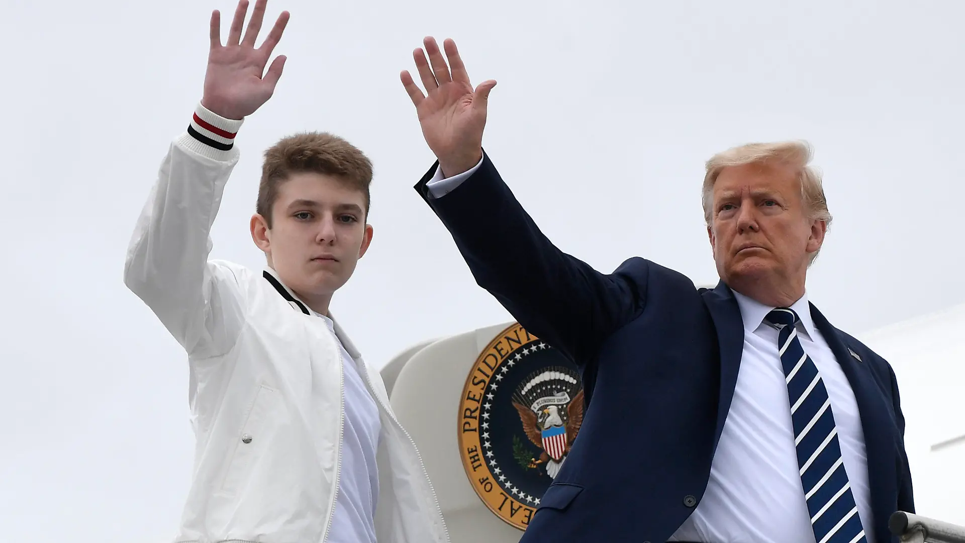 FILE - In this Aug. 16, 2020 file photo, President Donald Trump, right, and his son Barron Trump wave from the top of the steps to Air Force One at Morristown Municipal Airport in Morristown, N.J.  (AP Photo/Susan Walsh)